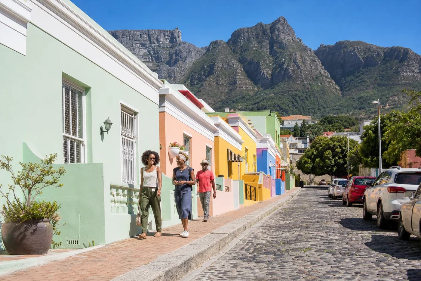 A sunlit Bo-Kaap street in Cape Town, painted houses and people walking, Table Mountain behind
